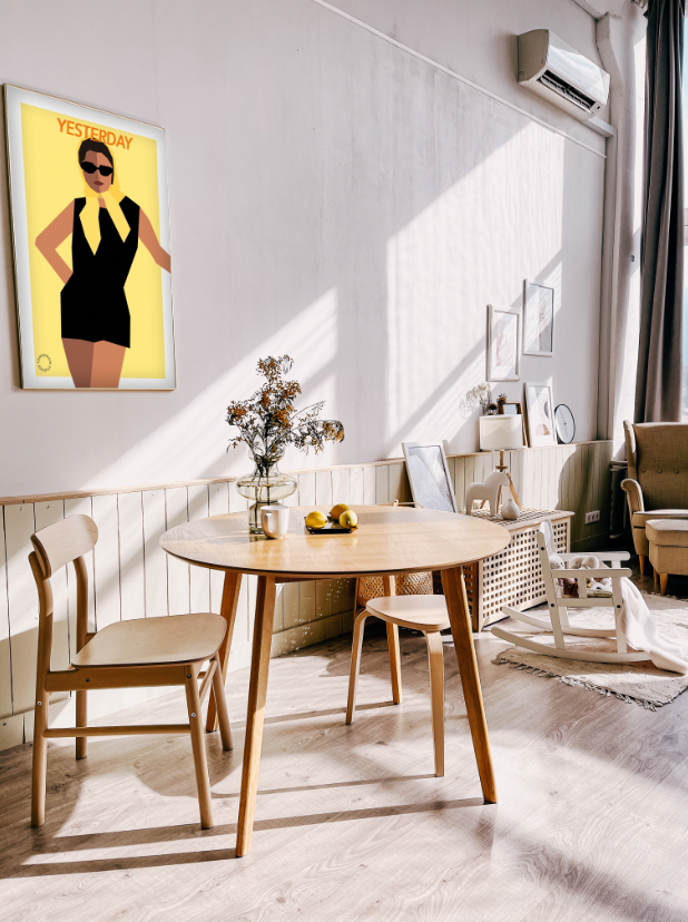 Lyst rum med et lyst spisebord med to stole ved. Over hænger der en Kreativ Kunstplakat i grafisk design af en kvinde med halstørklæde på hovedet og solbriller på.