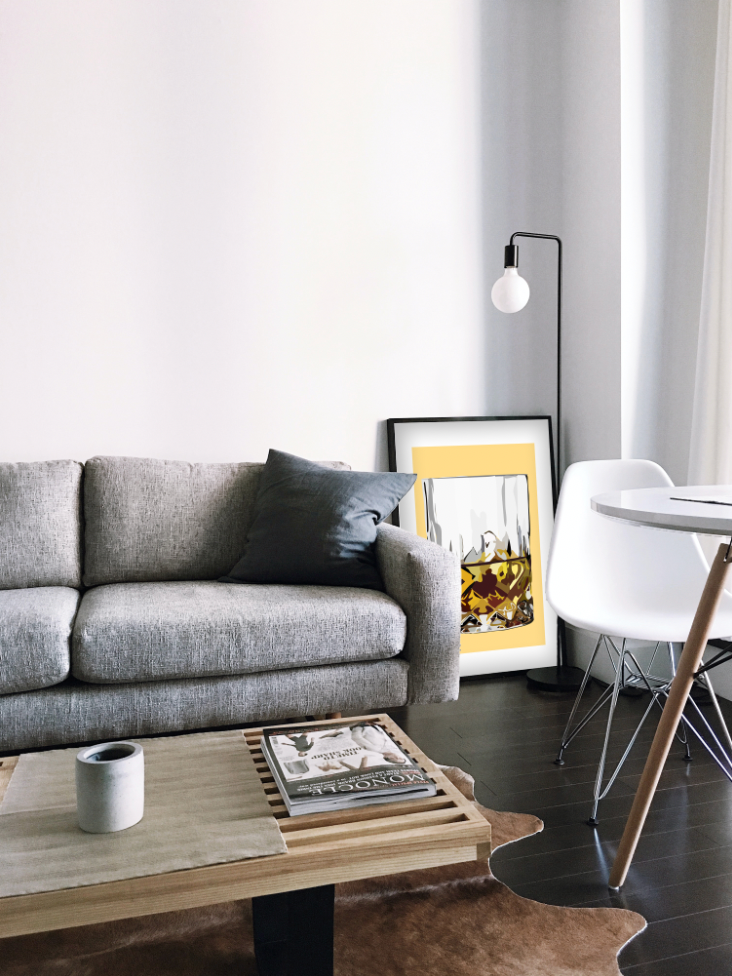 Stue med sofa, sofabord og en hvid stol. Der står en Kreativ Kunstplakat i grafisk design på gulvet af et whiskeyglas. 
