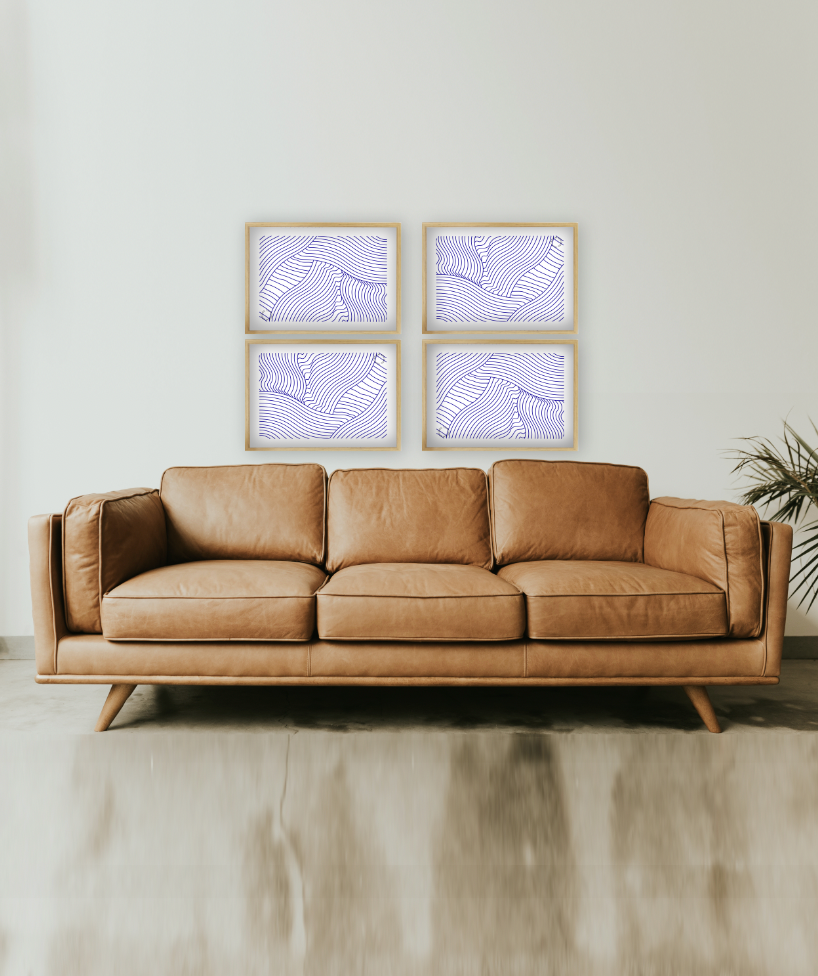 Sofa i lysebrunt læder i lyst rum, med fire Kreative Kunstplakater i grafisk design hængende over, i simpelt print med hvid baggrund og blå striber på